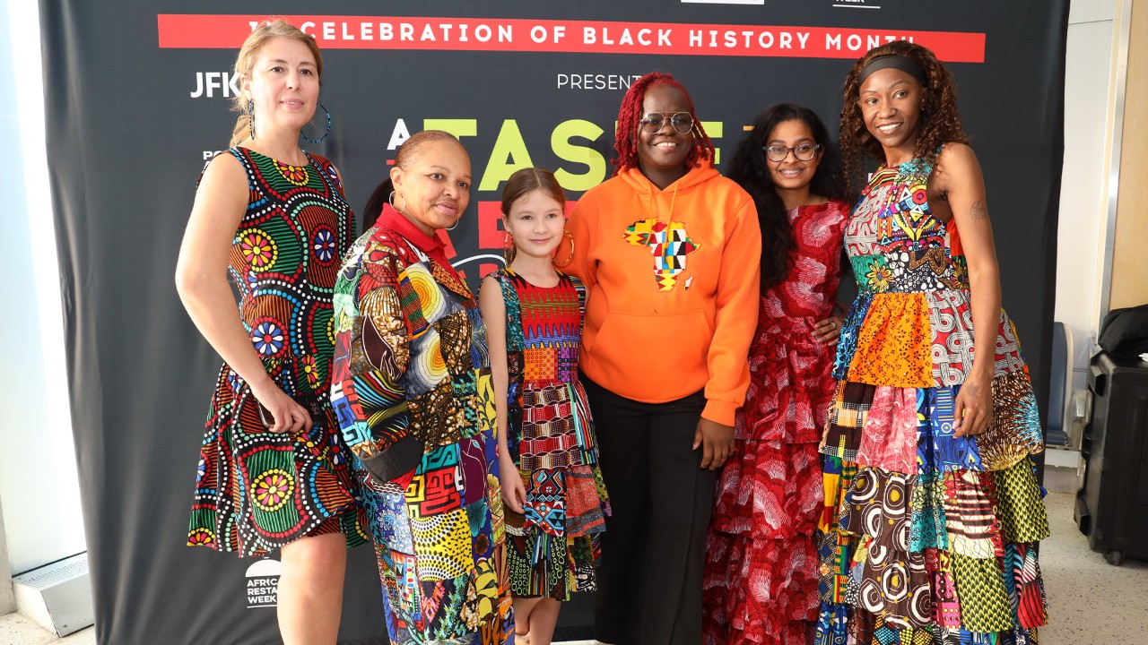 Women of all ages in brightly colored gowns smile at the camera